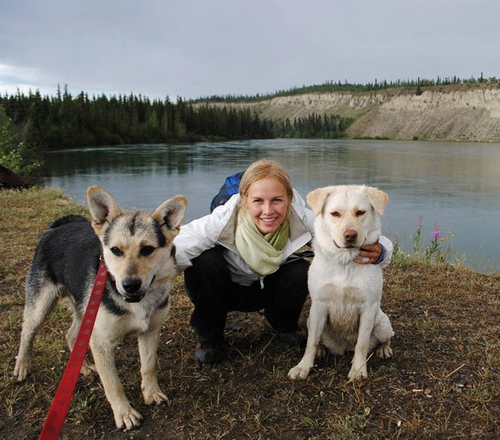 Fiona Emdin crouched in front of a lake with her two dogs. 