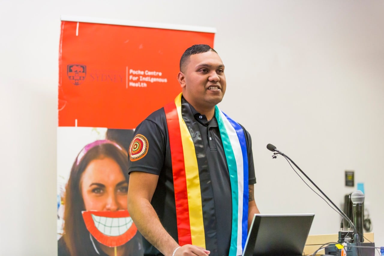 A photo of Paul Talbot, a proud Aboriginal man, speaking in front of a microphone.