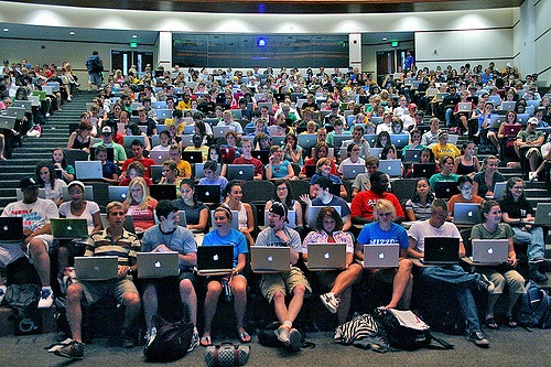 View of a lecture theatre taken from the teacher's perspective, with all students with laptops. The lecture theatre is full and the majority of laptops feature the Apple logo. 