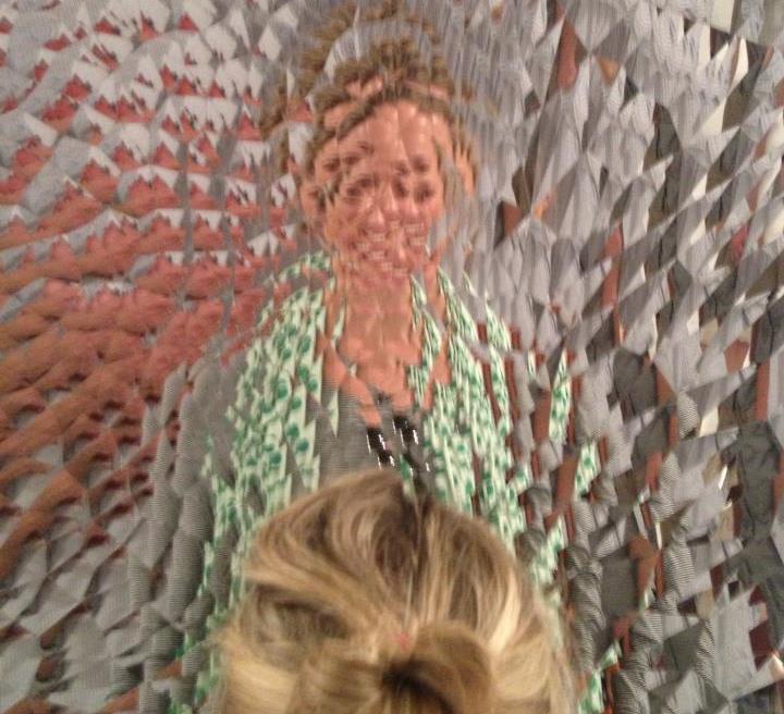 Woman looking into refractal mirror sculpture. Face is distorted and abstracted. 