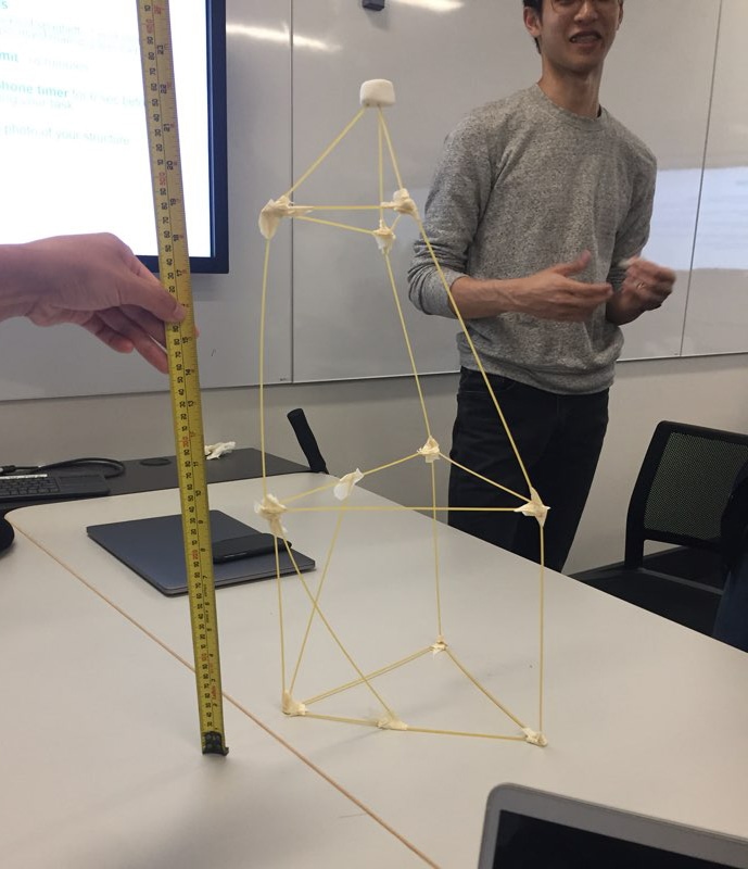 A student next to a marshmallow challenge structure that is being measured.