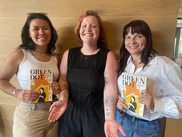 two alumni similing and posing with the author of Green Dot, Madeleine Grey, as they hold copies of the book.