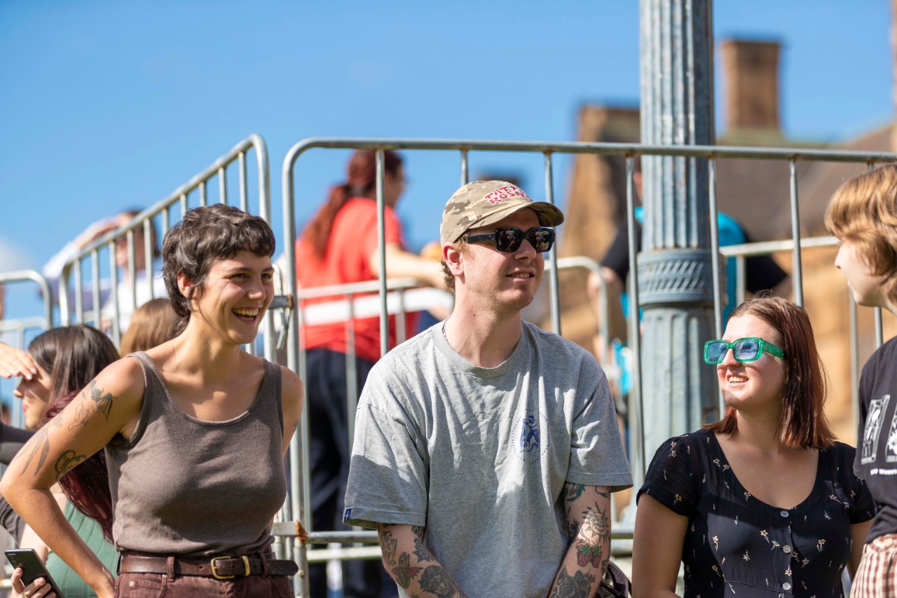 Three students standing against a metal fence facing and laughing towards each other.