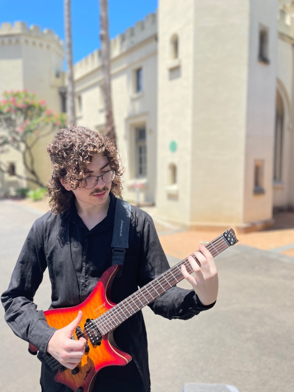 Alex Andrevski holding an electric guitar in front of the Conservatorium of Music building