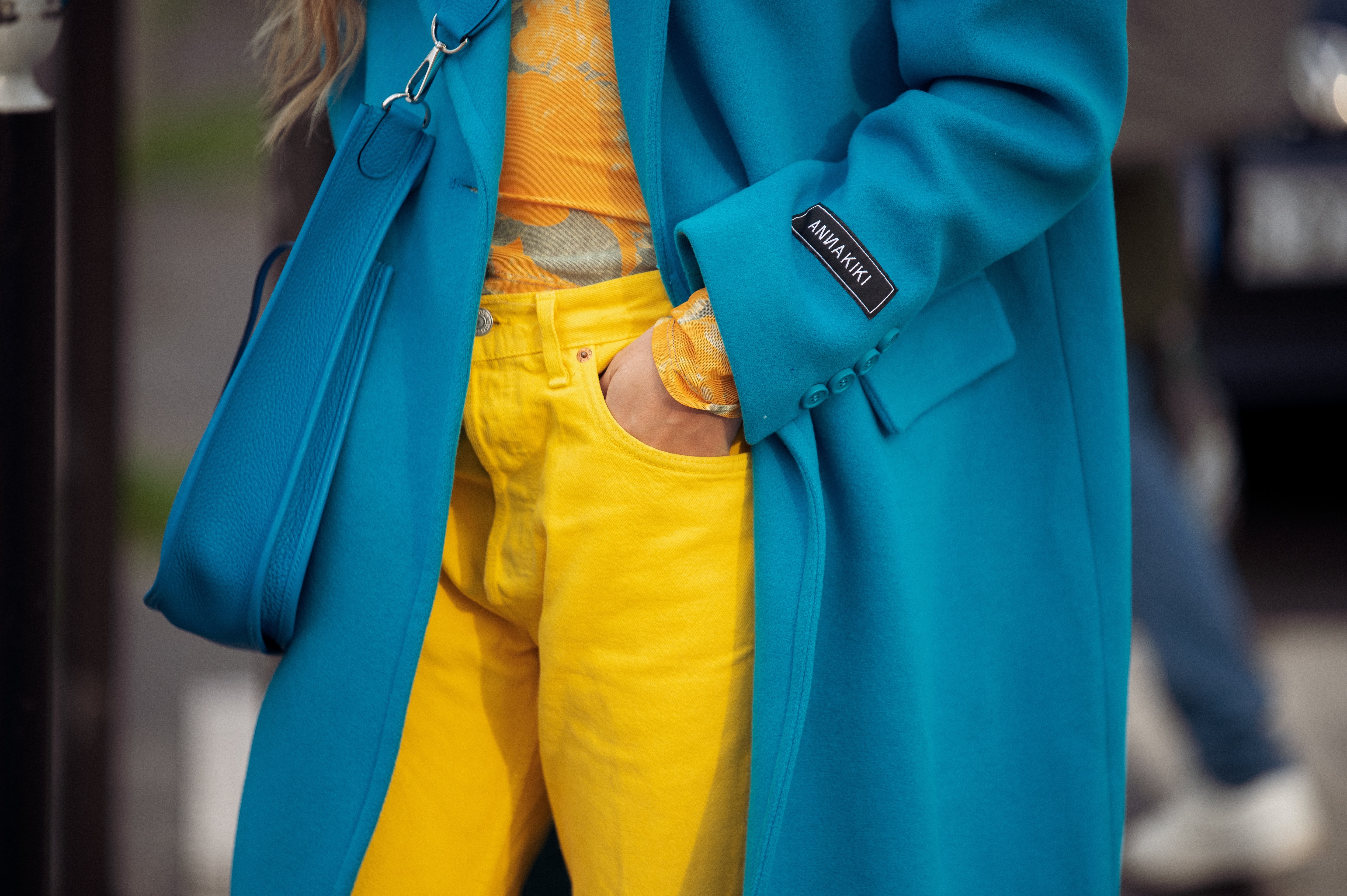 A guest in yellow pants, yellow shirt, and blue woolen coat is posing outside a fashion show in Paris fashion week Fall Winter 2022