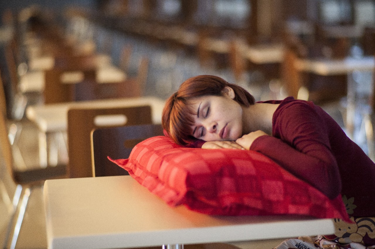 A woman sleeping with her head on a pillow on a desk.