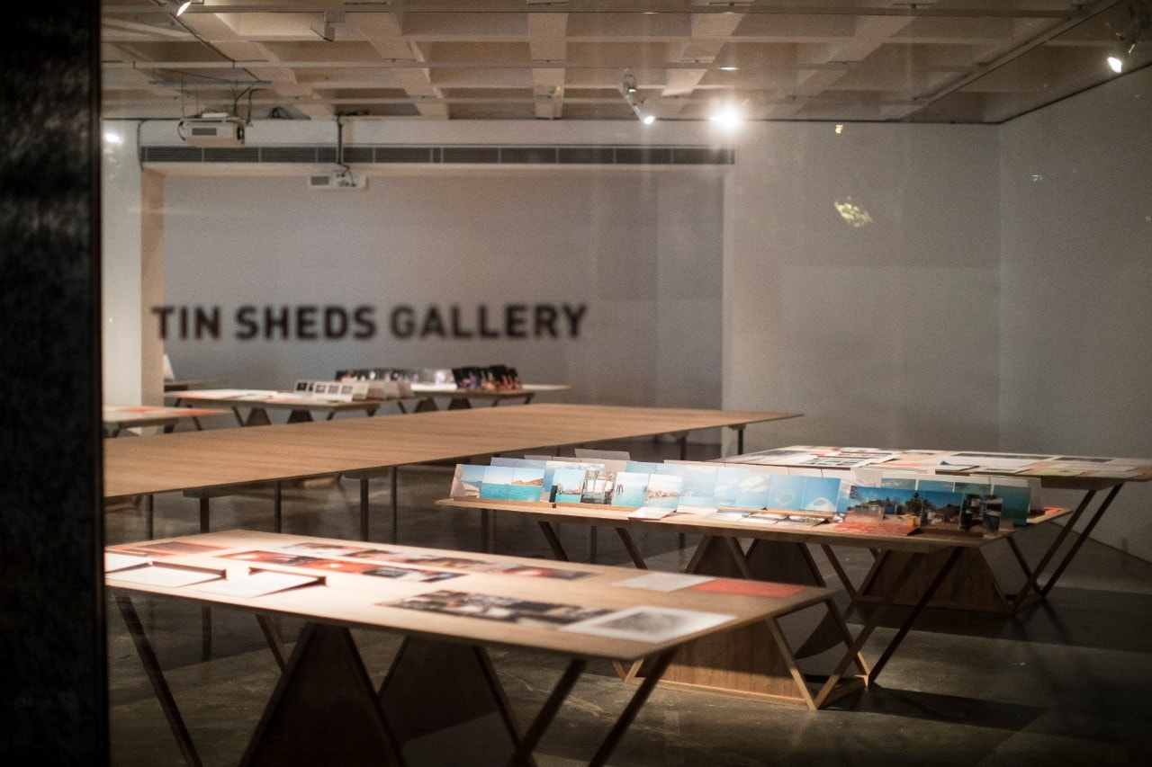'TIN SHEDS GALLERY' sign in the background of an exhibition featuring serveral photographs.