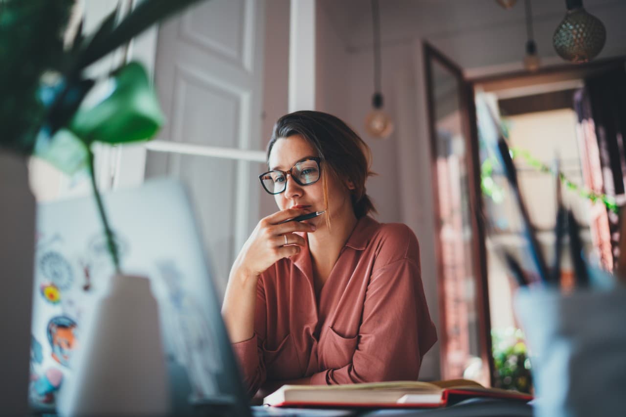 Woman sitting in front of a laptop holding pencil