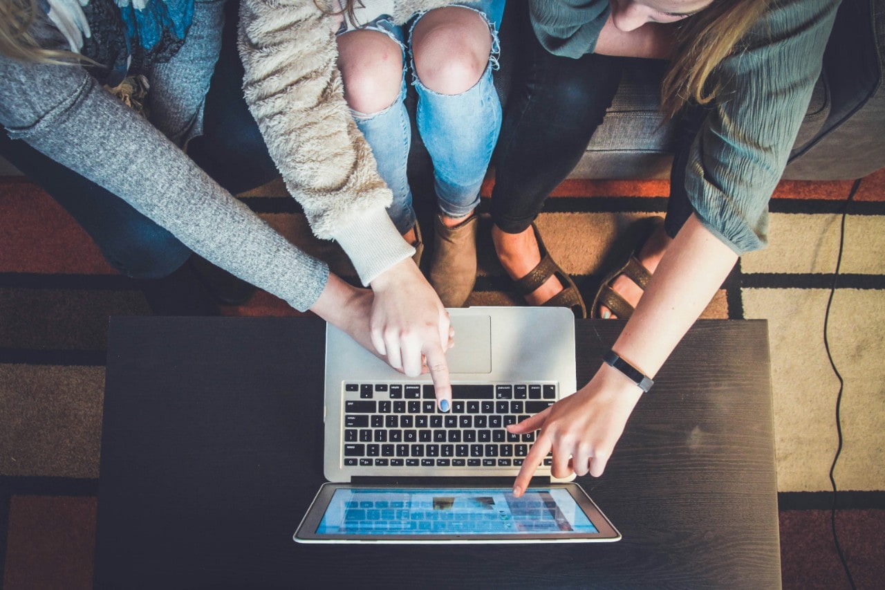 Three people sitting down and pointing at a laptop screen. Image by John Schnobrich on Unsplash.