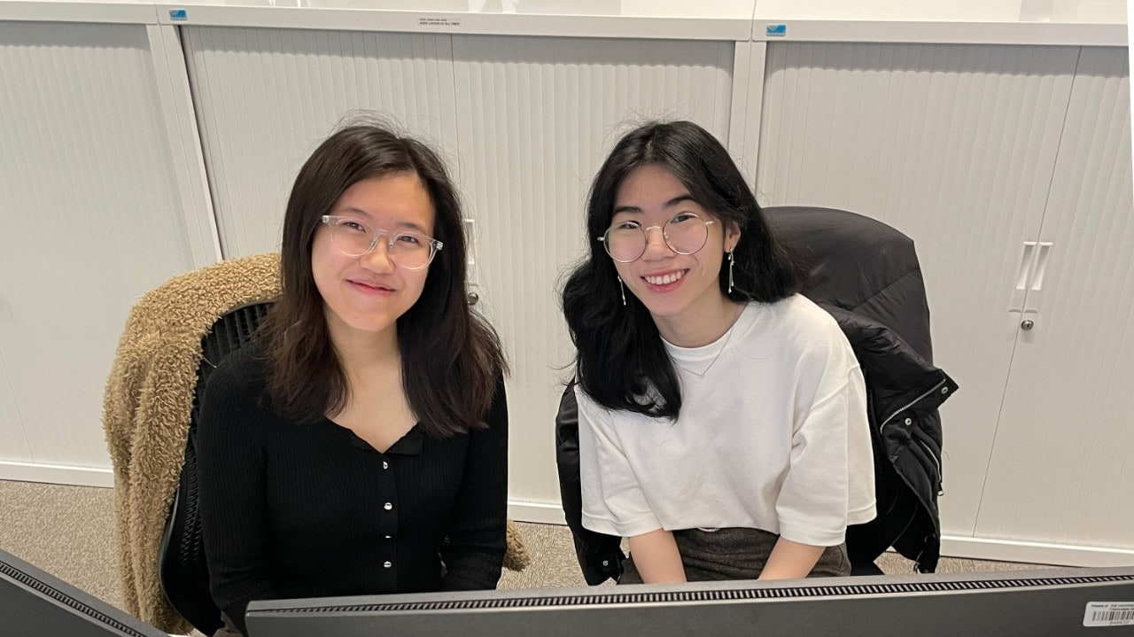 Two girls sat behind a computer, smiling