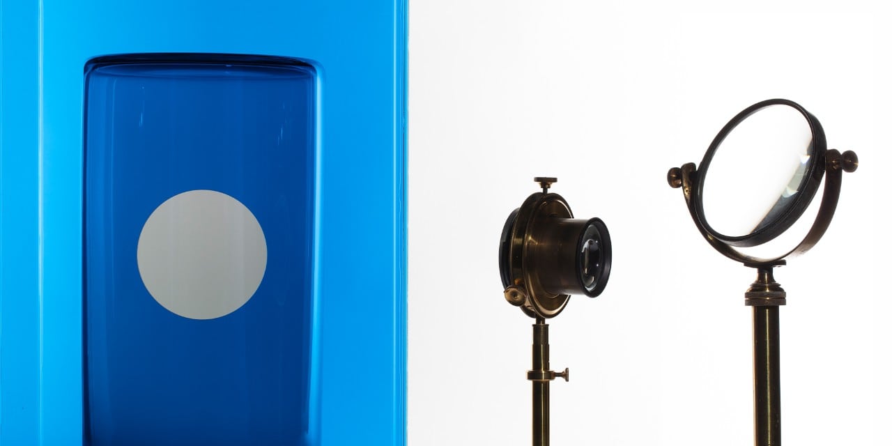 Blue artwork on left side, optical equipment on right side.
