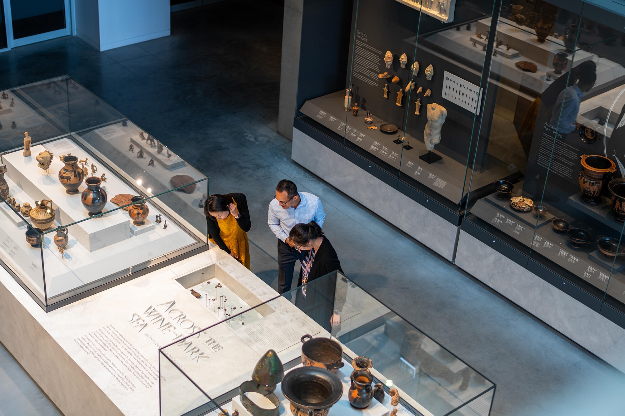 Three people look into the cabinets as part of the Mediterranean Identities exhibition