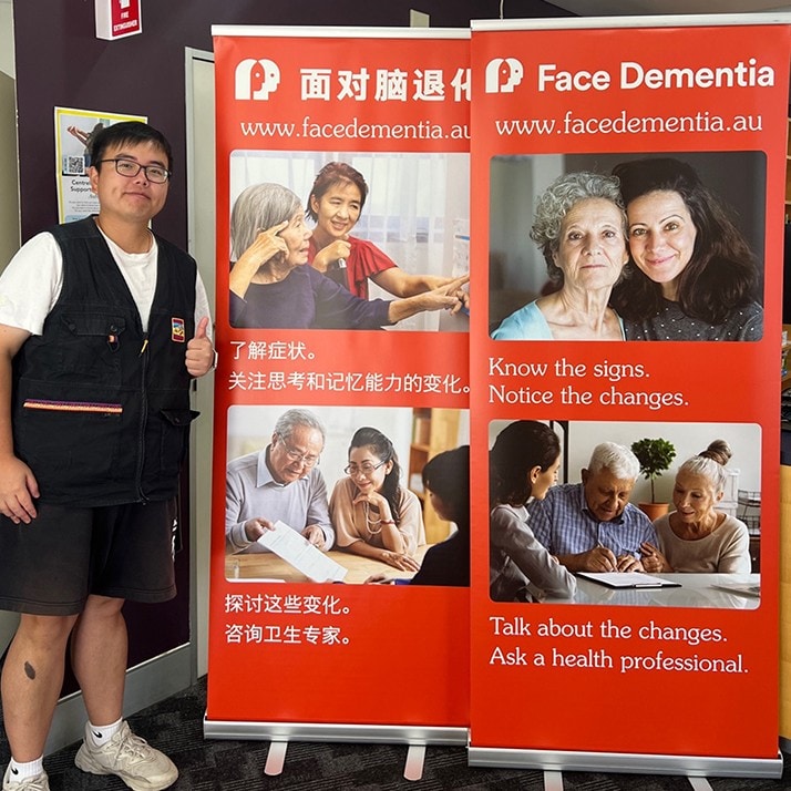 A man standing next to banners at a Face Dementia community event