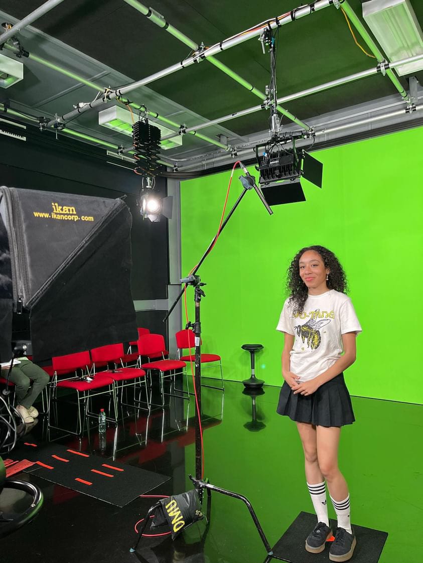 Kaela in the studio against a green screen recording social media content for the University