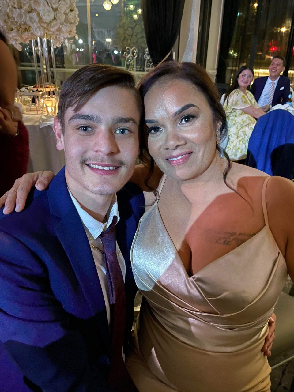 Dylan (right) with a woman at an event. He is wearing a blue suit with a white shirt underneath. 