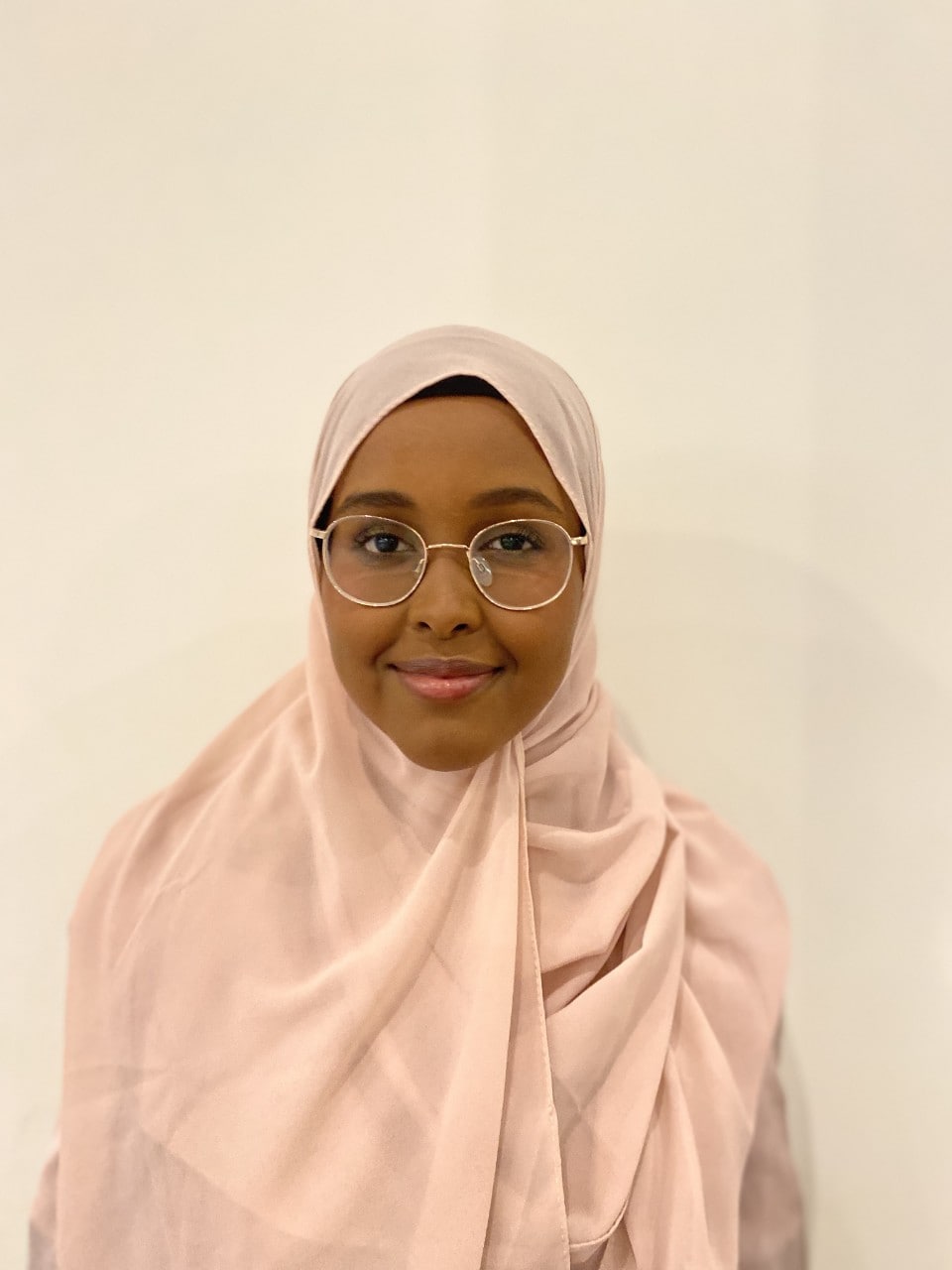 Mariam is looking directly at the camera and is wearing a matching pale pink shirt and headscarf. She is smiling