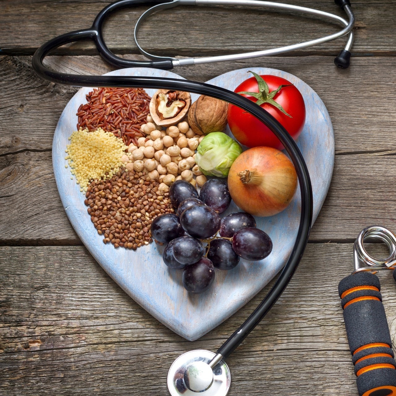 Heathly food arranged on a heart-shaped plate surrounded by a stethoscope and gym gear