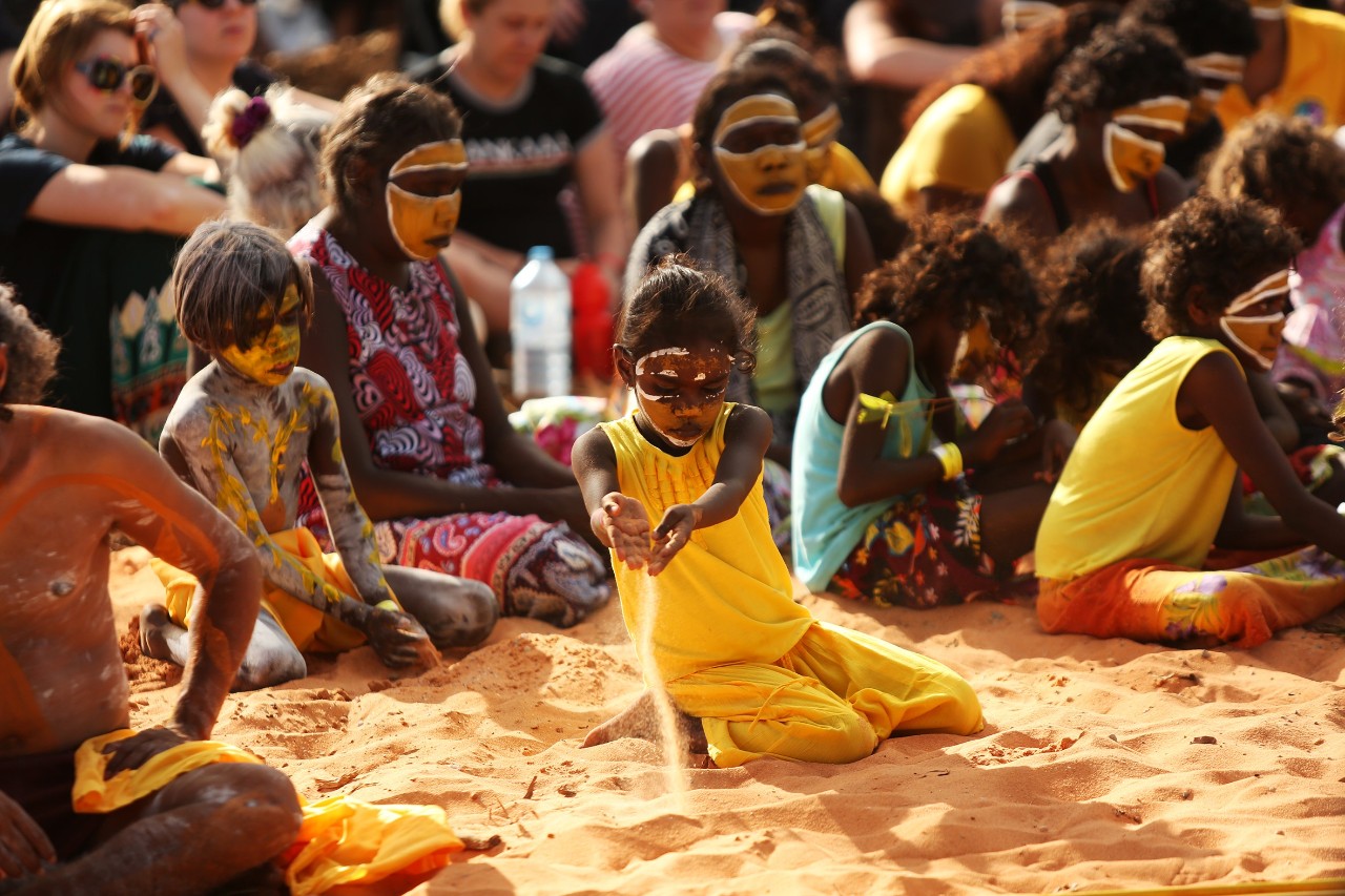 A photo of Aboriginal people in traditional dress sitting on the ground.