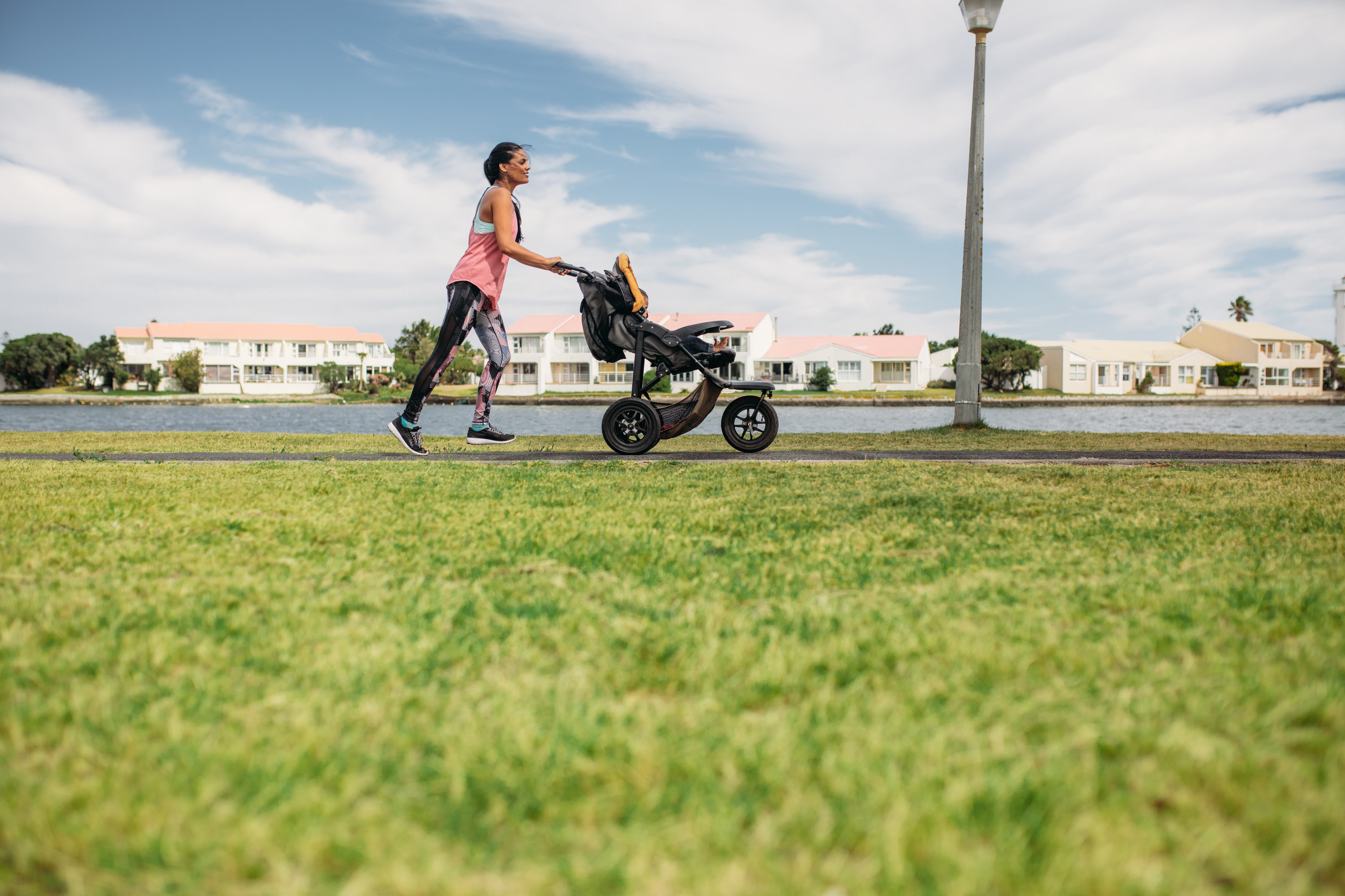 Young mother jogging in park pushing a baby pram. Active mom staying fit by running with her baby in the stroller.