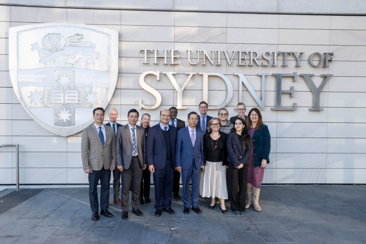 Delegation of the Vietnamese Ambassador meets with University representatives in front of the University logo.