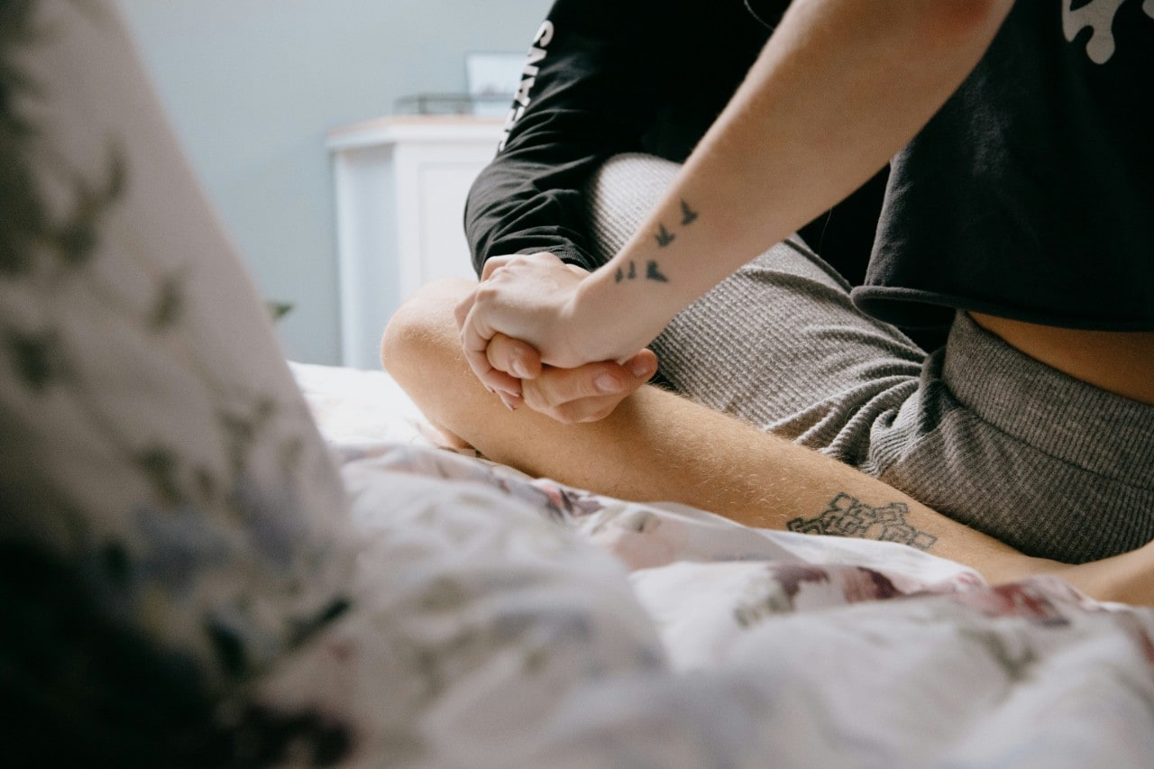 Two people sitting close together and holding hands on a bed.