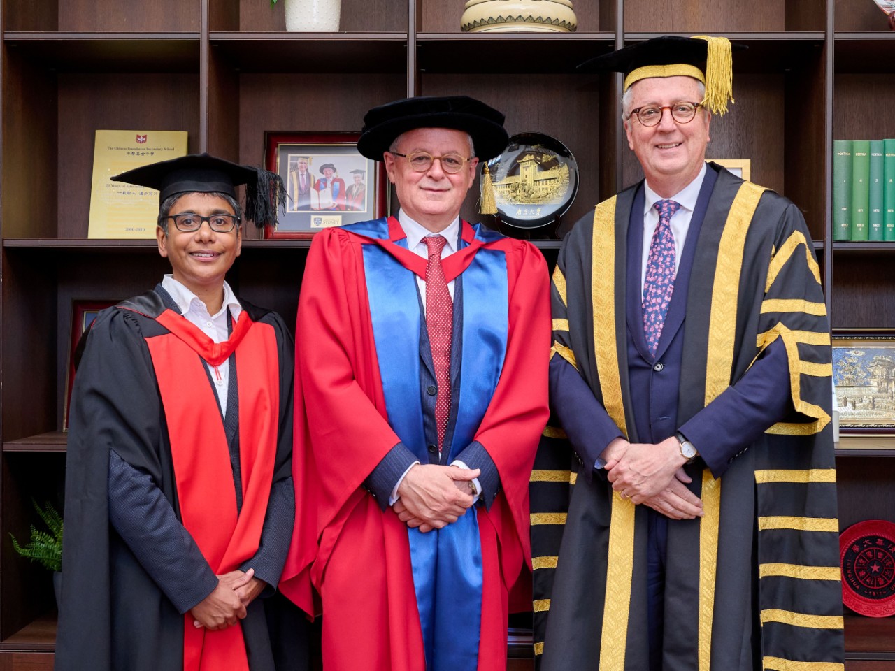 Three people in academic regalia in front of a shelf