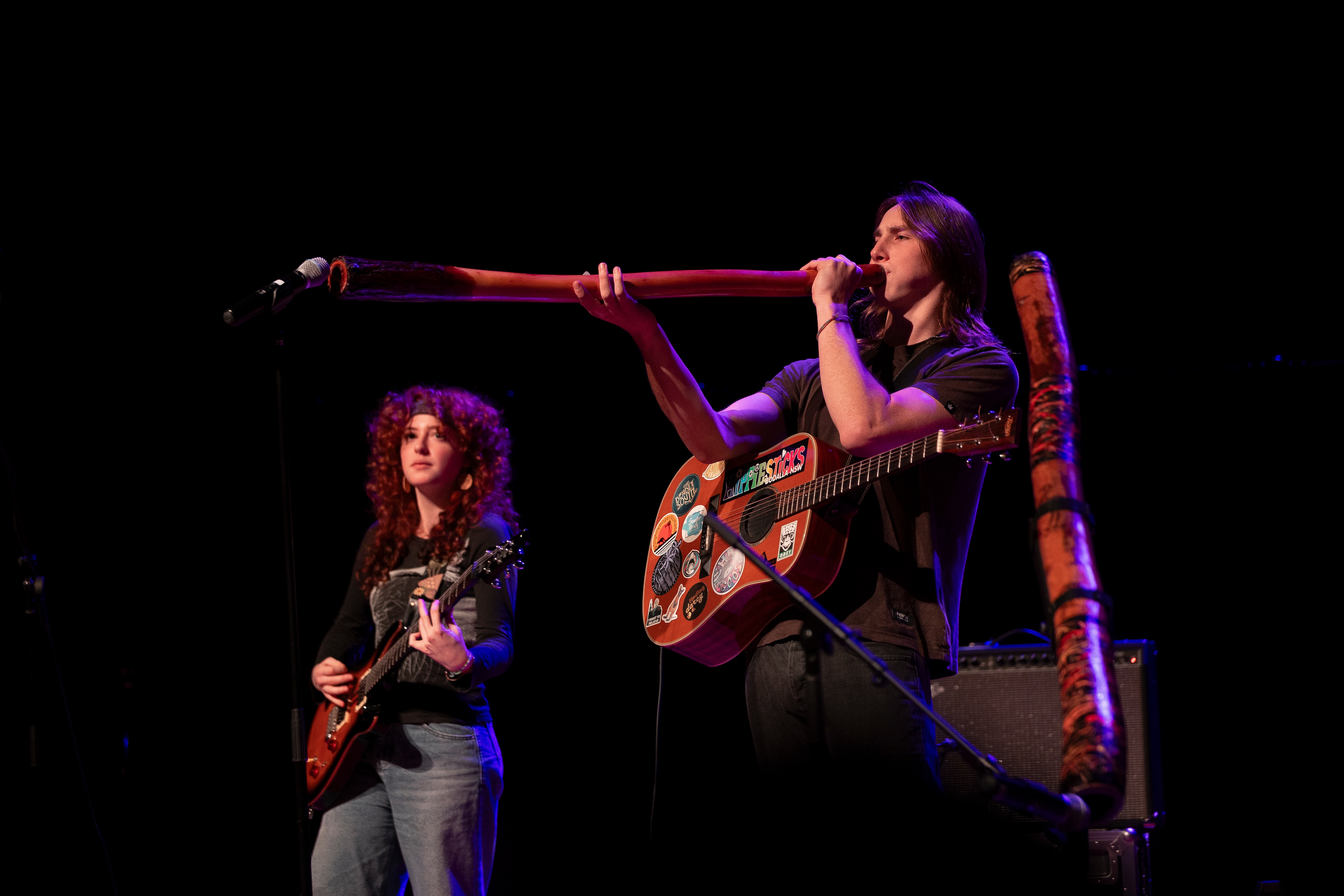 Jake on stage playing yidaki (didgeridoo) with his band, Lemonise with a band member on guitar beside him.