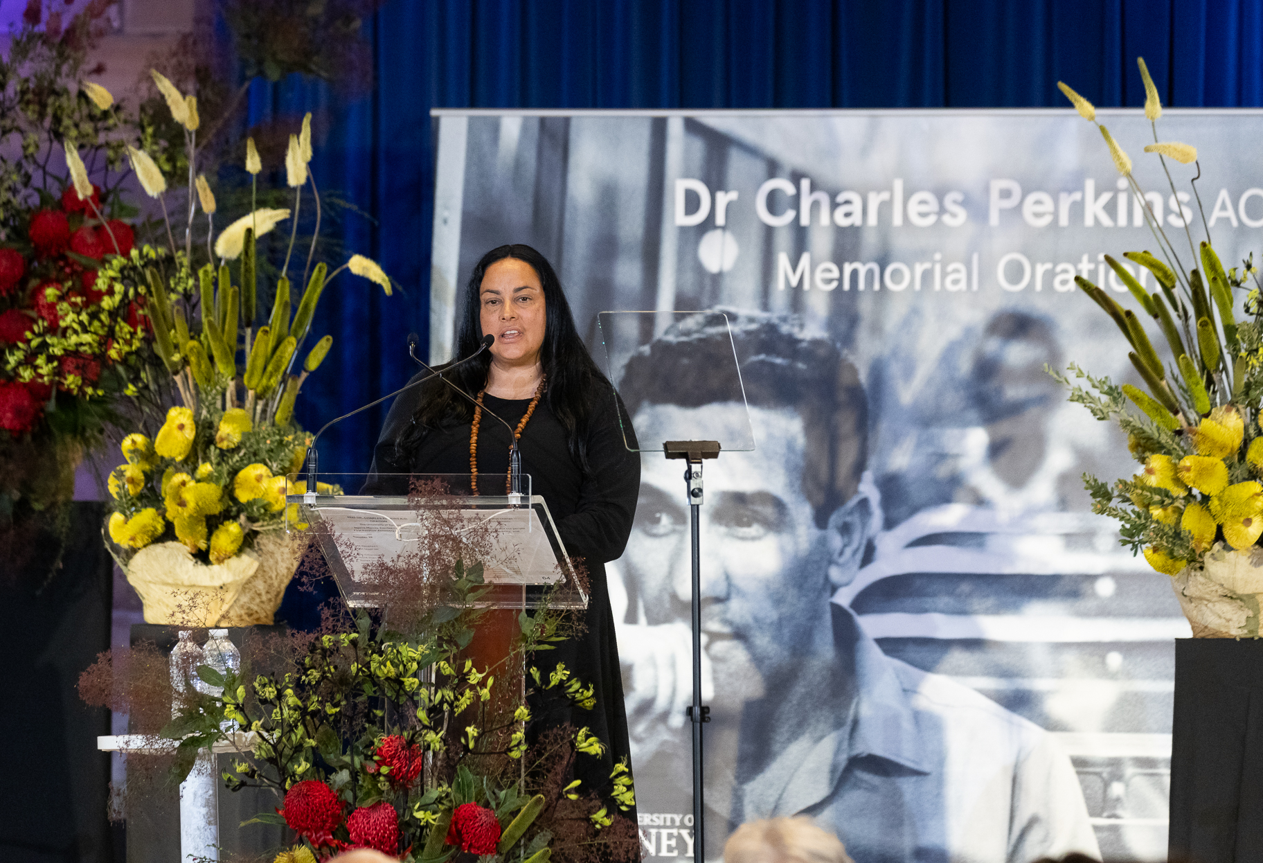 Woman at a podium with flowers and a media banner behind her