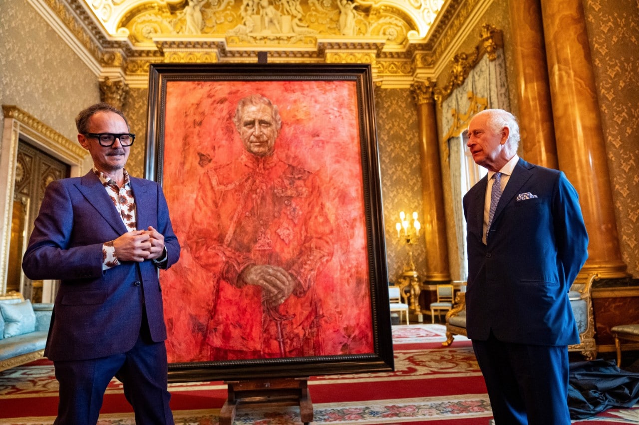 an artist standing next to his painting of King Charles III with Charles looking on