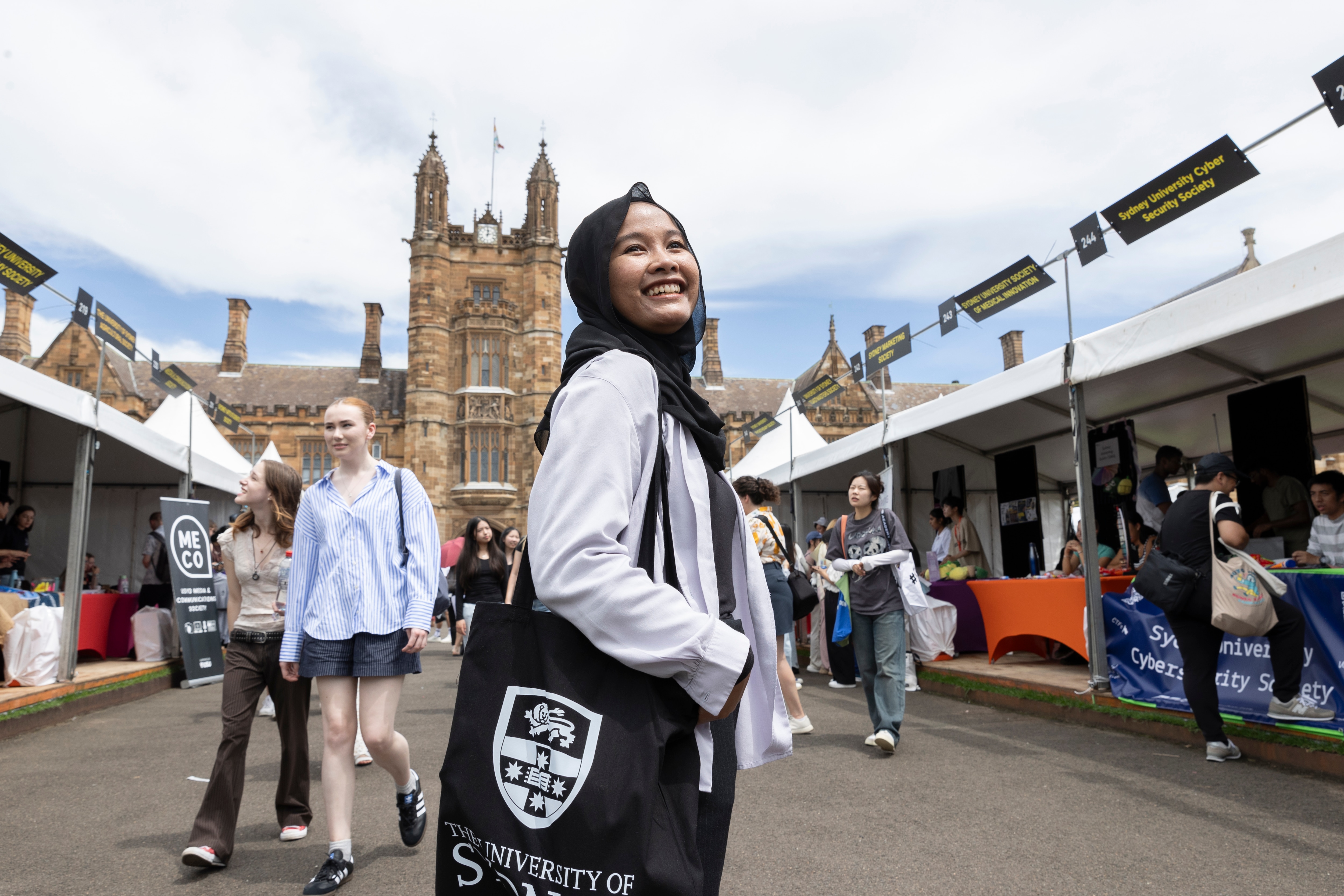 A new student at Welcome amongst stalls on the lawn in front of the quadrangle