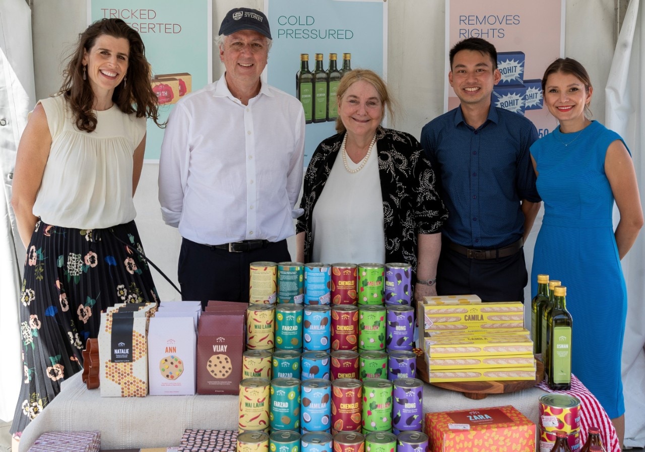 Five people standing in front of a stand of groceries