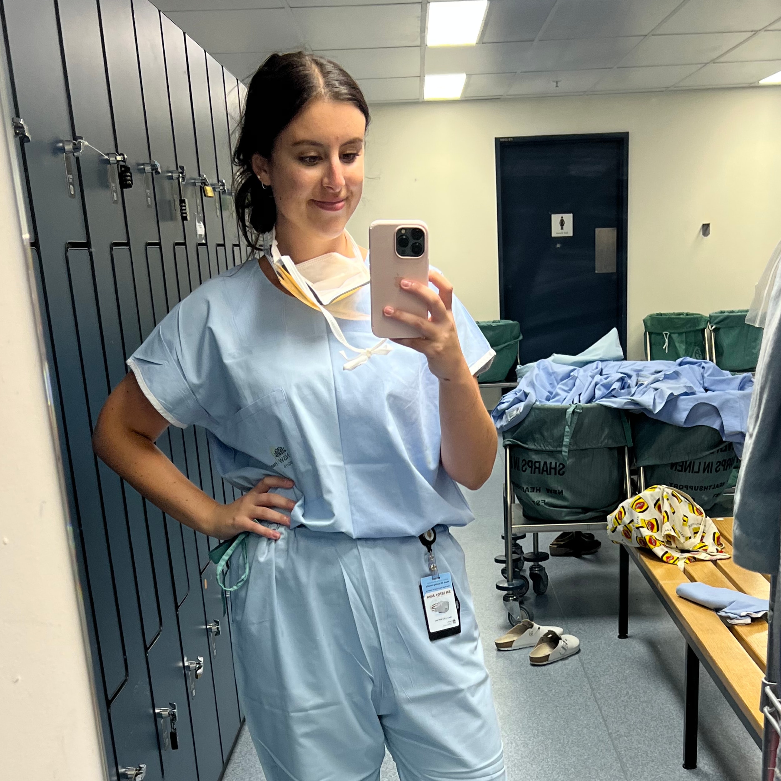 Maddi in her medical scrubs in a changeroom looking at her phone.