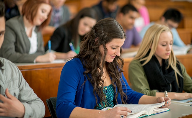 A multi-ethnic group of college age students are sitting in a lecture hall working on an in class assignment.