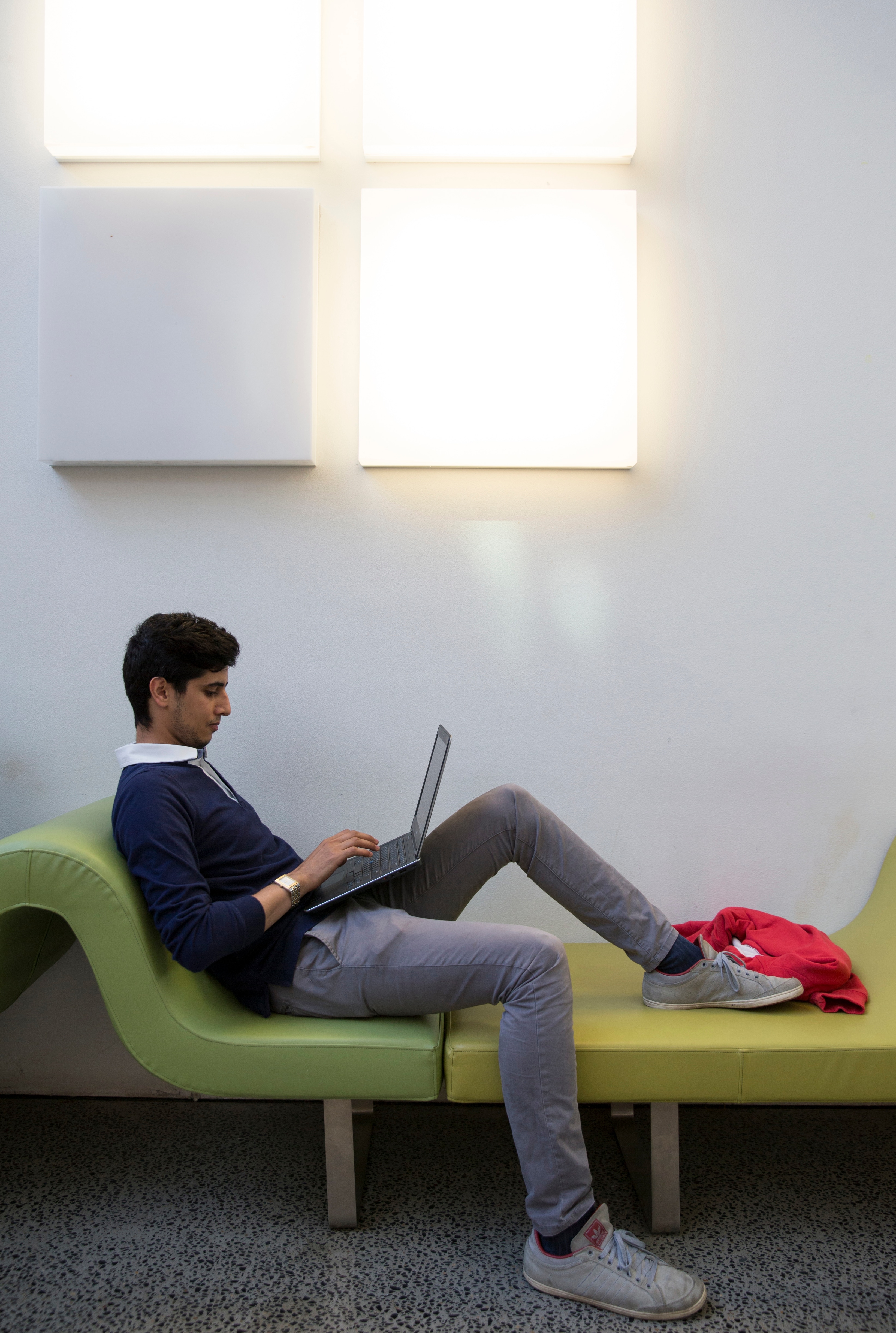 Student sitting on green lounge with laptop.