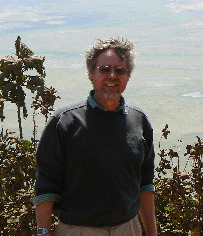 Graham Jew standing on a hill with Tanzanian plains and water points in the background