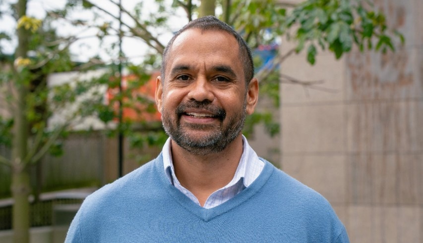 Photo of Michael Doyle, Bardi man and Associate Professor, Sydney Medical School. He is in front of a building with foliage in frame.