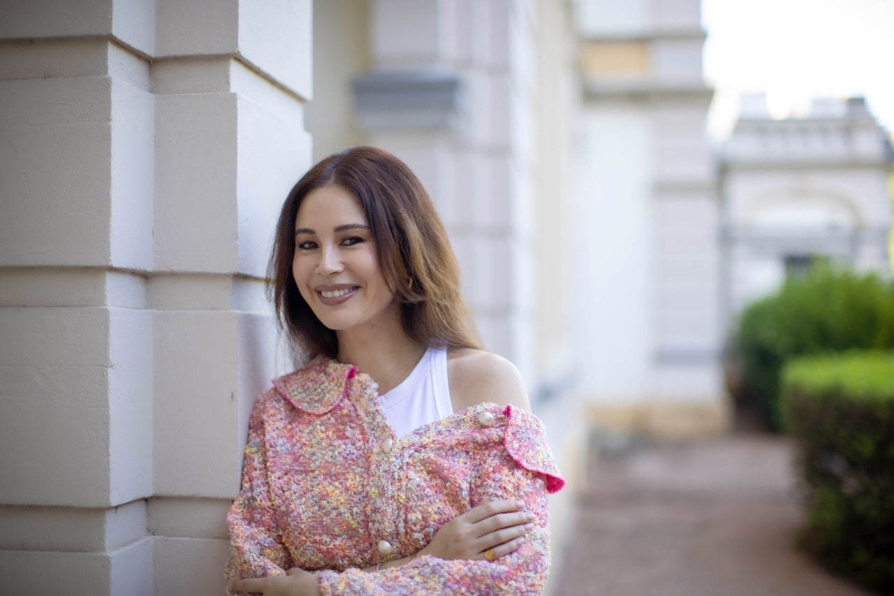 Yvette smiling while posing and leaning against a wall.