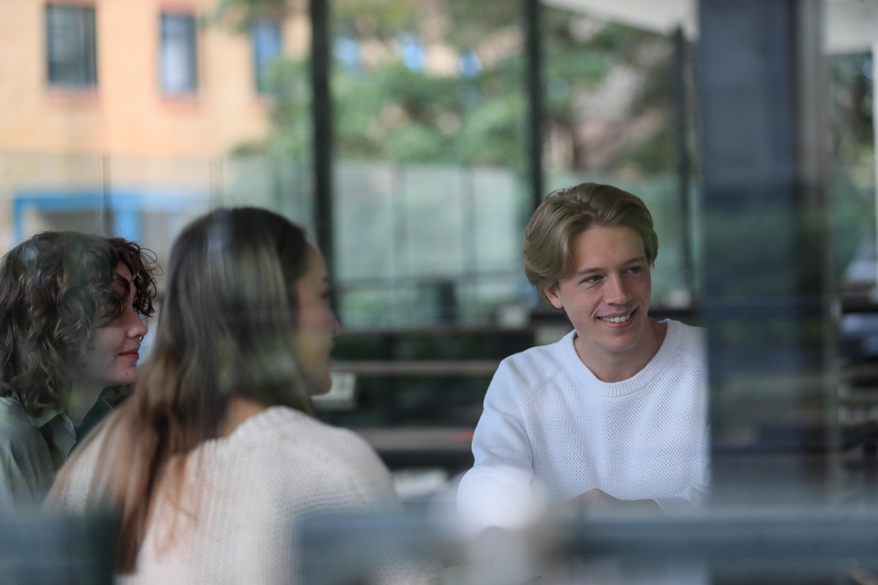 Students talking while seated at a table inside Brennan Maccallum Building.