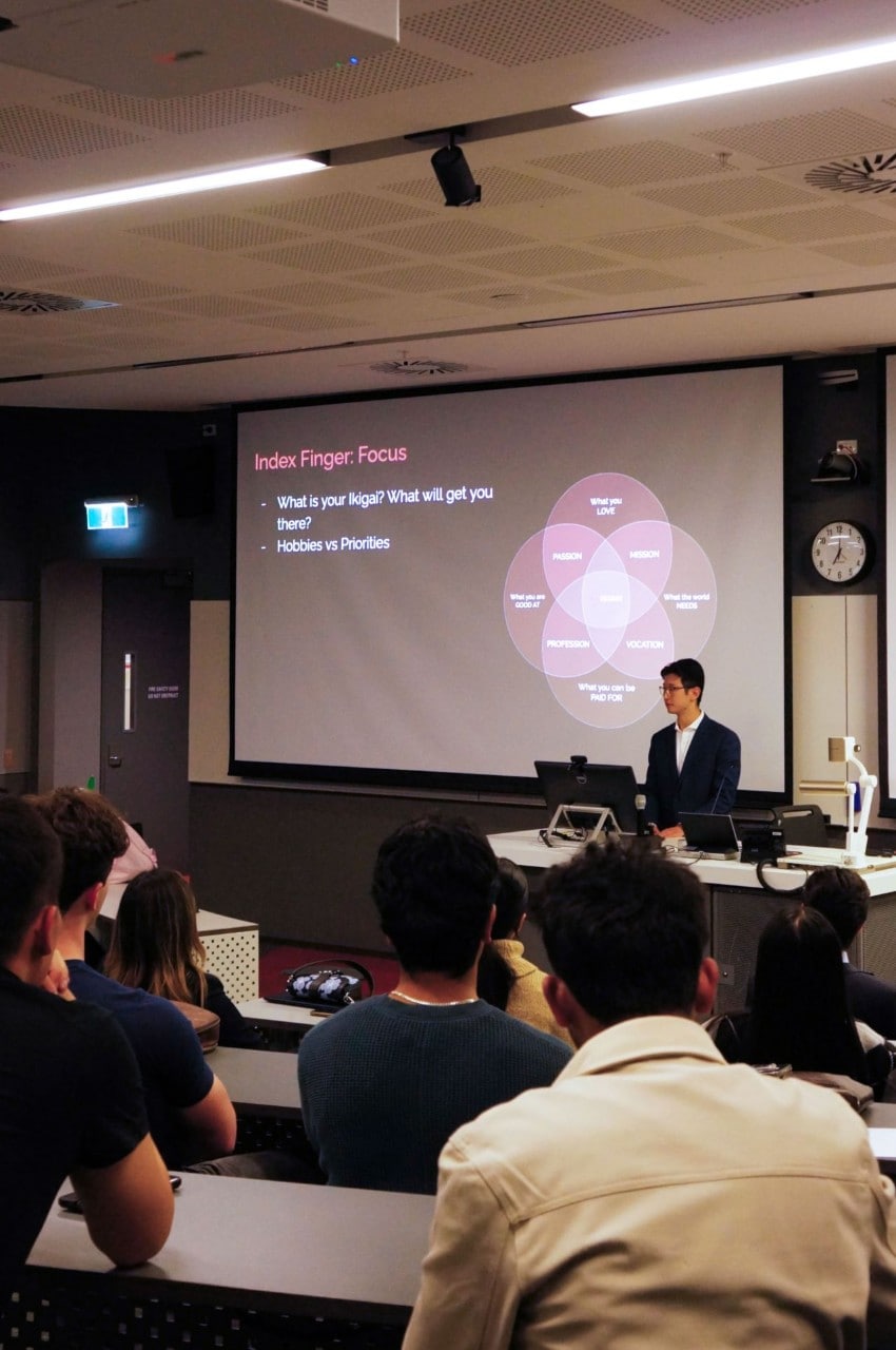 A classroom with Jason Zhu He delivering a slide presentation from a lectern. 