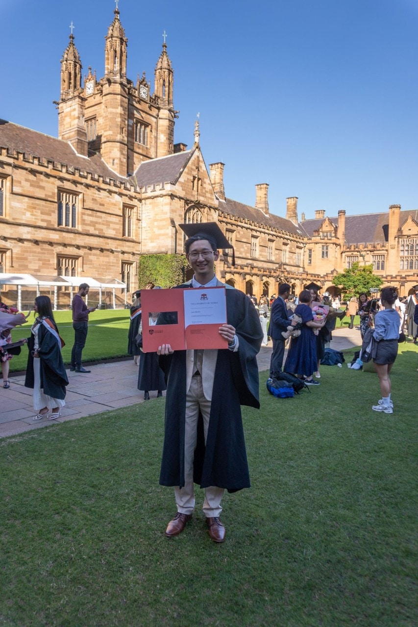 Jason Zhu He at a University of Sydney graduation ceremony holding his testamur for a Bachelor of Science.