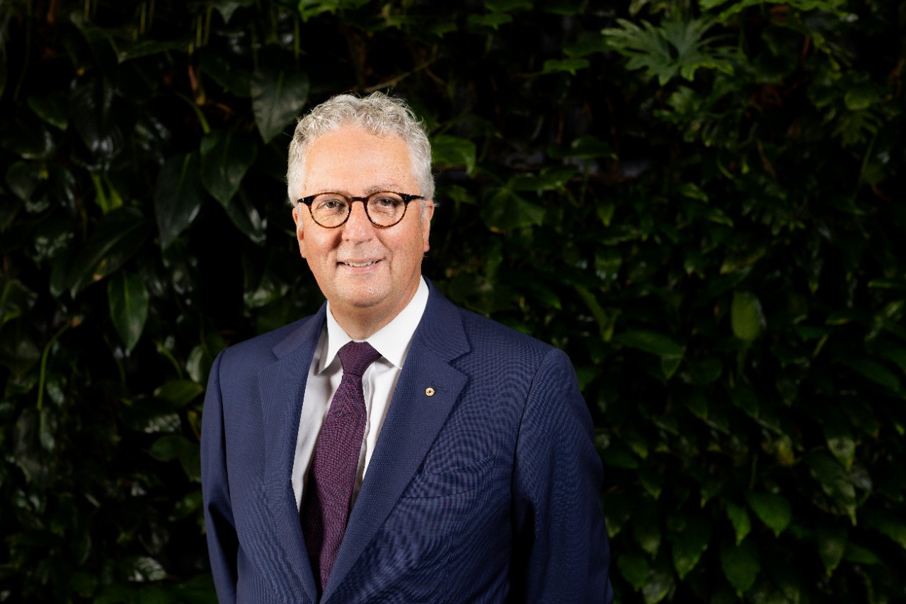 Professor Mark Scott stands in front of a wall of climbing plants, wearing a dark blue suit