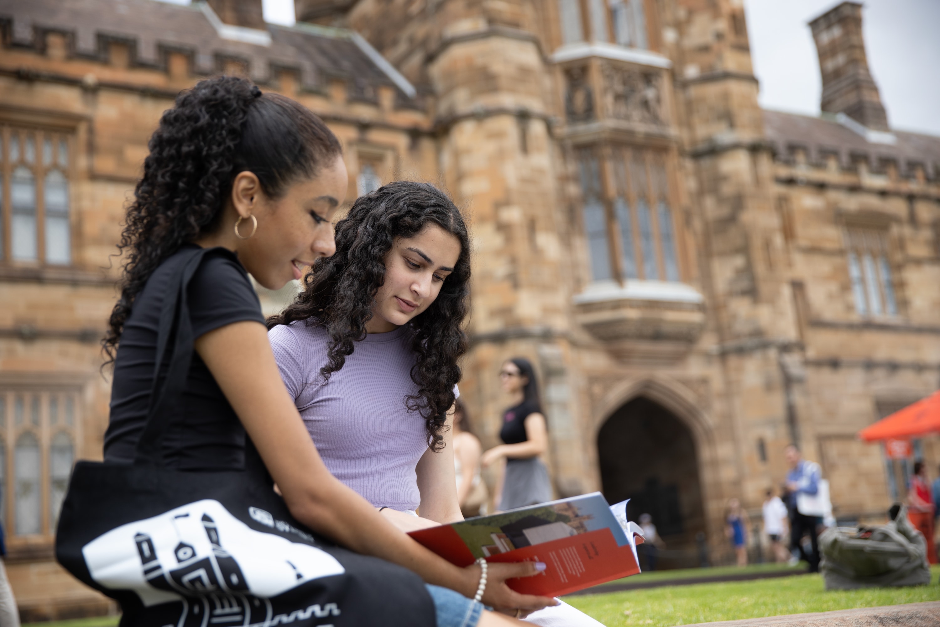 Two people looking at a booklet on the lawn outside the quadrangle