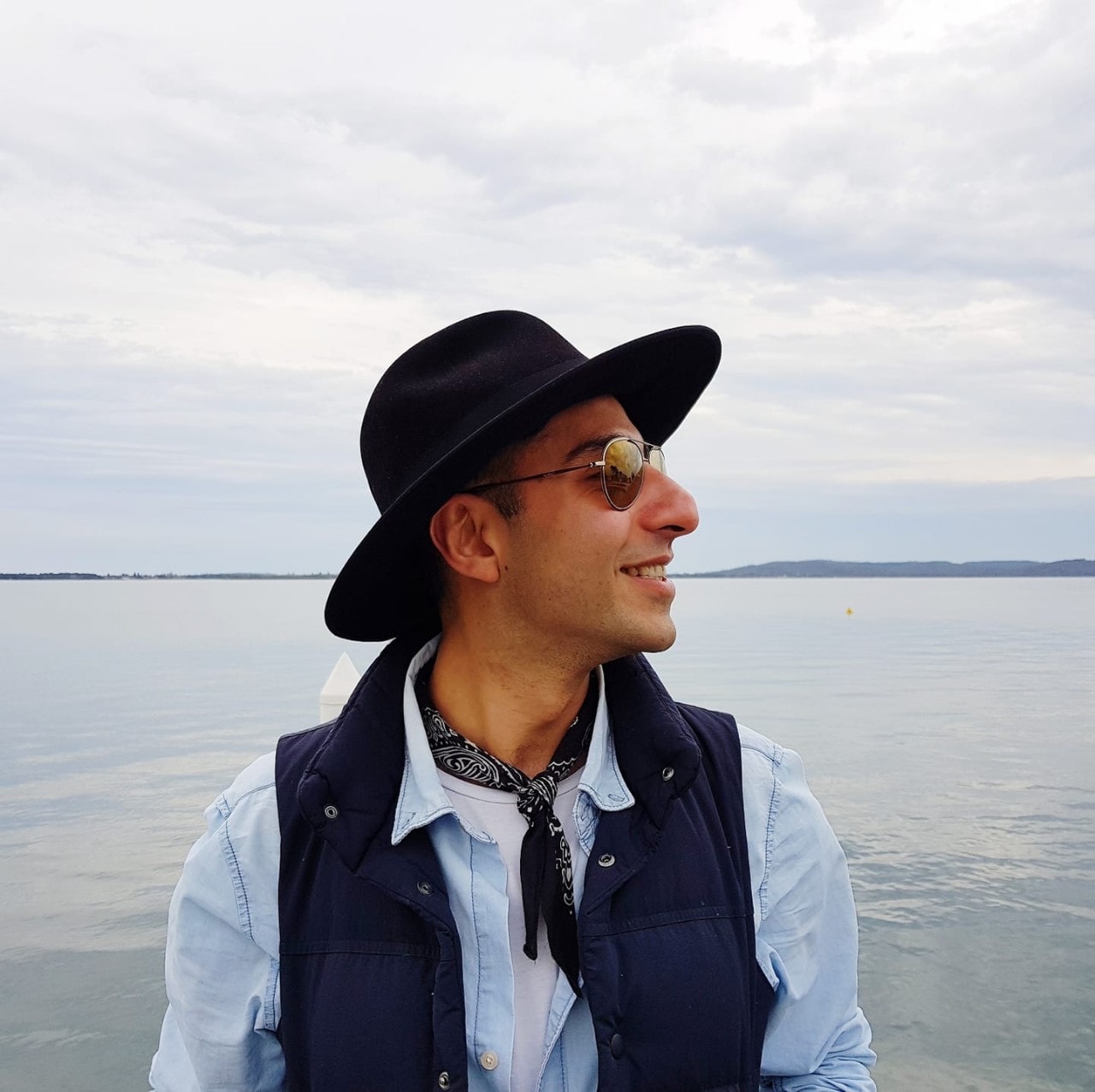 Ali Asghar wearing hat and sunglasses, side-on, with water in background