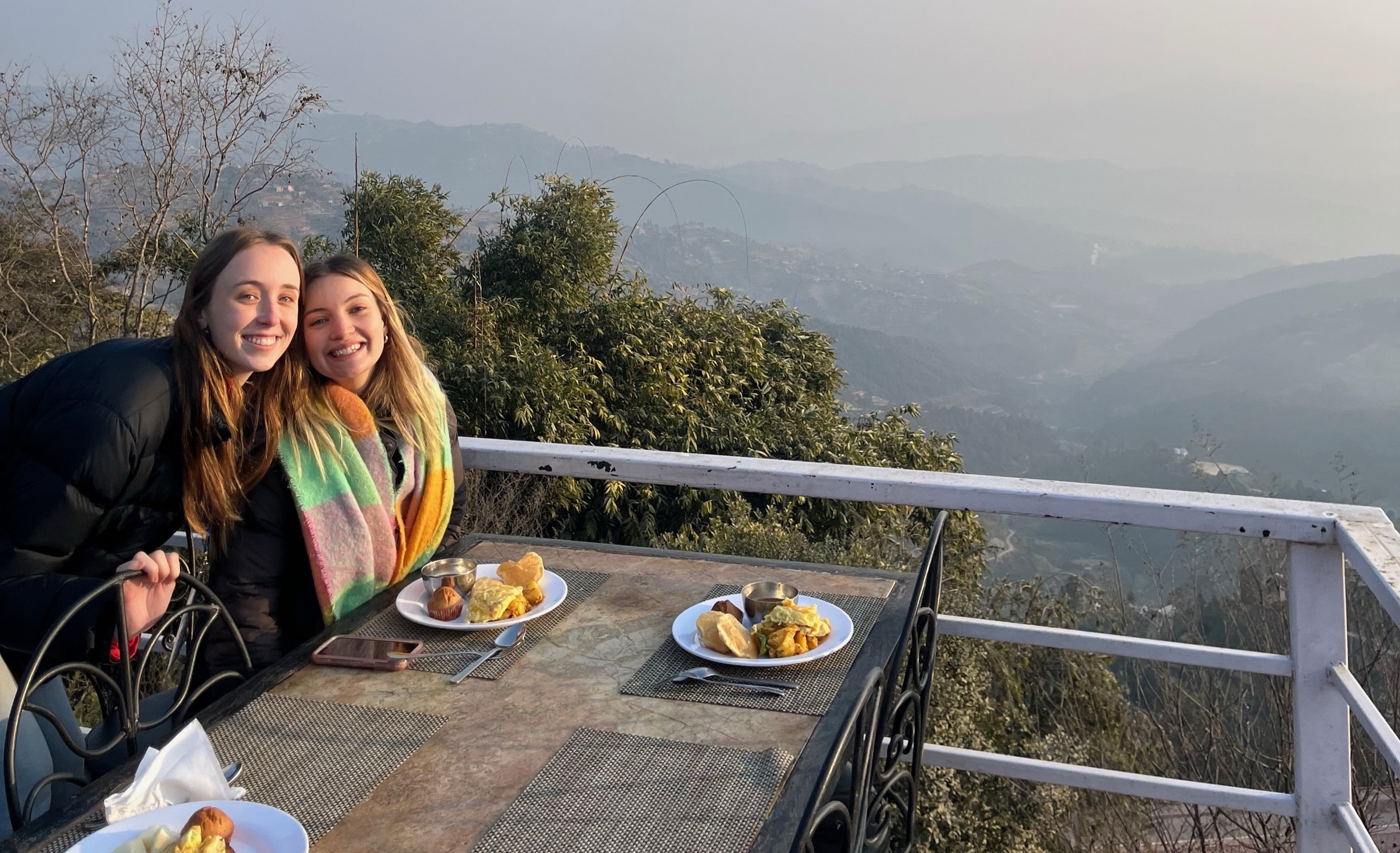 A pair of female students enjoying breakfast with a view of the Kathmandu mountains