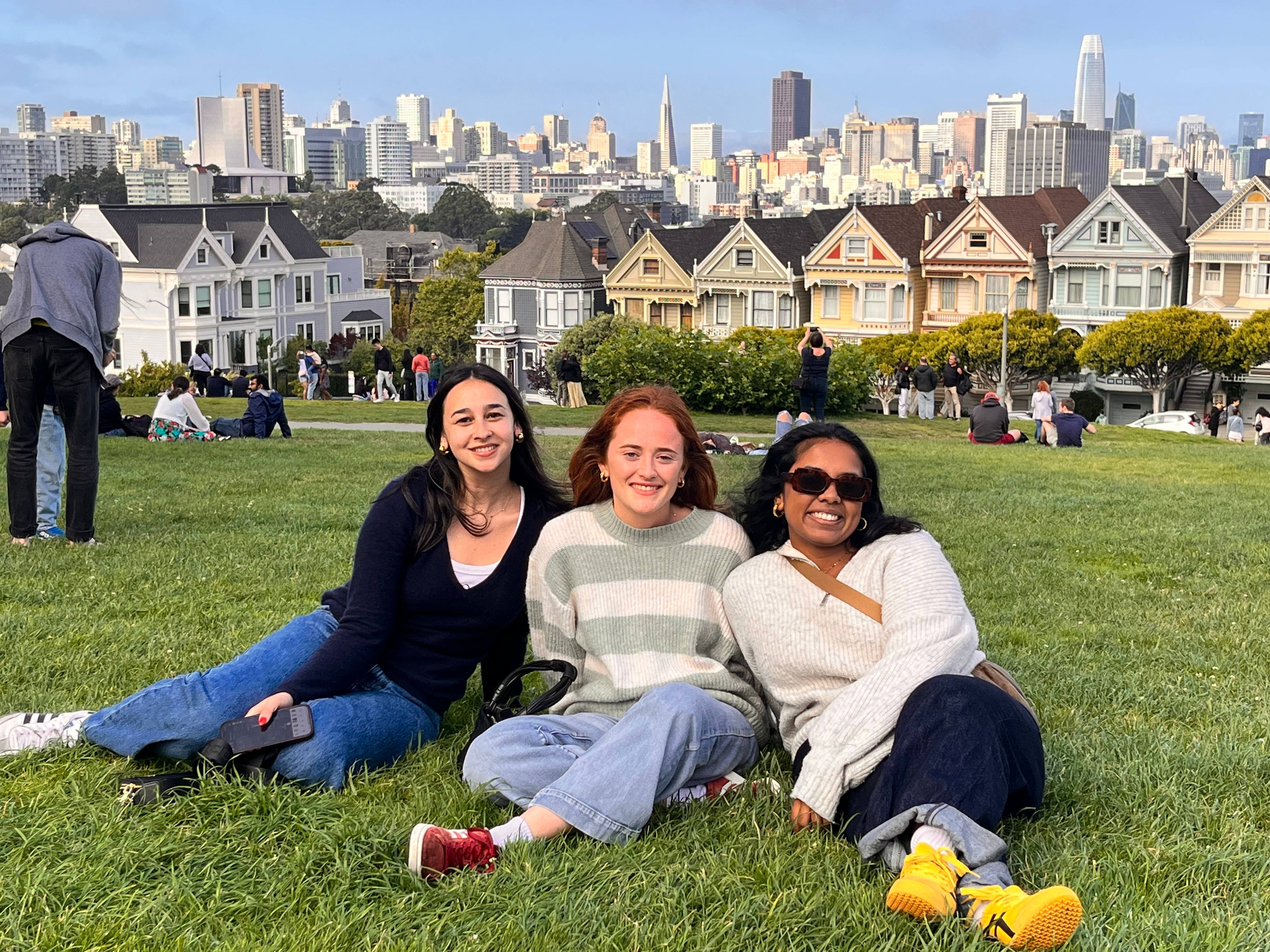 Three female students lounging on the Painted Ladies greens in San Francisco, California