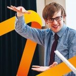 Man in glasses wearing blue shirt and maroon tie gestures to another person (who is out of frame) while being surrounded with the orange logo of the Higher Education Academy
