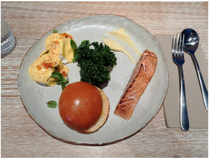A dinner plate with eggs, hollandaise sauce, parsley, grilled salmon, and an apple on it.